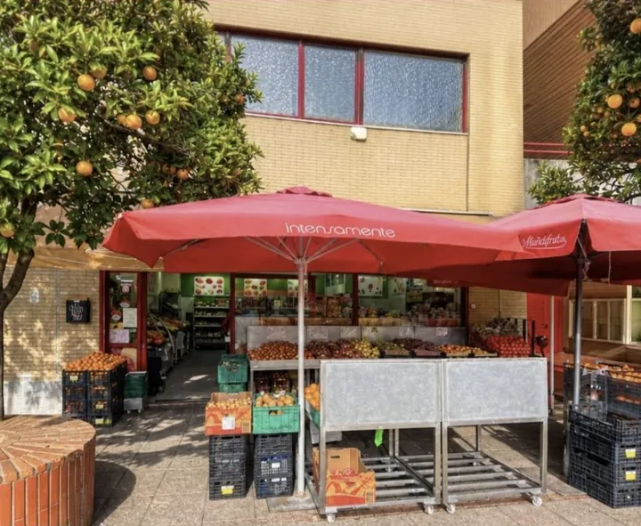 Fachada da loja MUNDIFRUTA no Centro Cívico de Carnaxide, com bancas de fruta e chapéus vermelhos